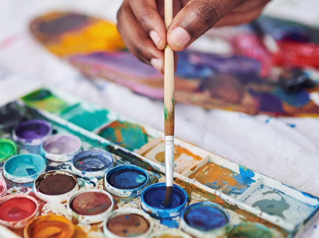 Close-up of a hand dipping a paintbrush into a watercolor palette during an art therapy session
